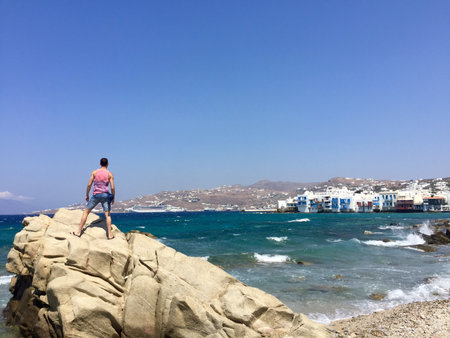 A closeup shot of a young male standing on the cliff near the sea in Mykonos, Greeceの写真素材