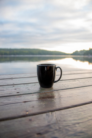 A vertical shot of a black mug on the wooden pier of the lake
