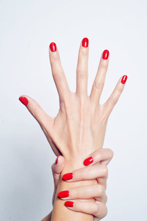 A vertical closeup shot of female hands with red nail polishの写真素材