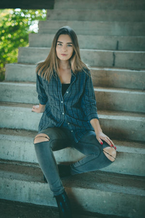 An attractive Bosnian Caucasian woman sitting on a staircase of an abandoned building