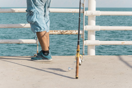 A closeup shot of a man putting his fishing rod on the ground and waiting for fishesの写真素材