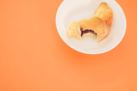 A bitten croissant on a white plate isolated on orange backgroundの写真素材