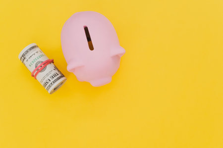 A top view of a pink piggy bank and dollar bills isolated on a yellow backgroundの写真素材
