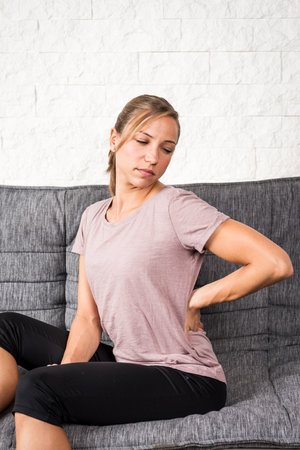 Young blonde woman has back pain during sportsの写真素材