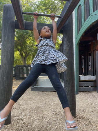 A  vertical shot of a young black girl swinging from monkey bars in a children's playgroundの写真素材