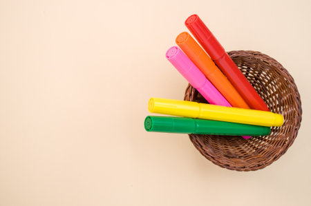 A closeup shot of colorful markers on a small woven basket isolated on a pink backgroundの写真素材