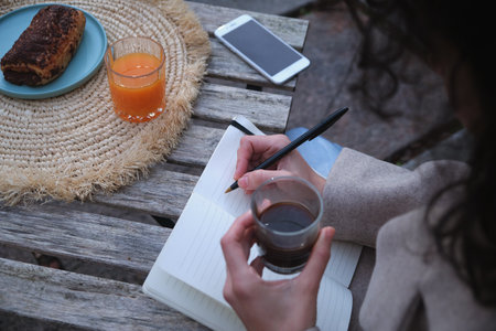 A high angle view of a woman having breakfast and writing in her notebook sitting outsideの写真素材