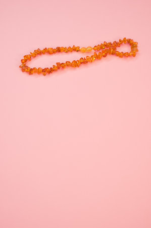 A closeup shot of an amber beads necklace on a pink surfaceの写真素材
