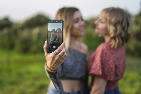 A shallow focus of young Caucasian friends taking a selfie with the back camera of the phone in a parkの写真素材