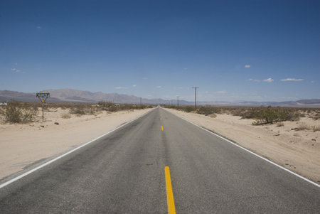 Long straight asphalt road through desert landscape of Death Valley, California