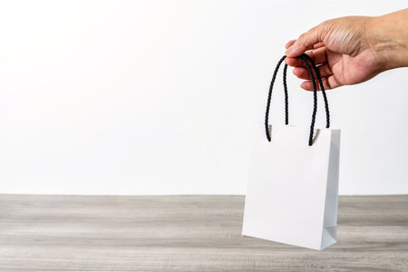A hand holding white shopping paper bag over a wooden tableの写真素材