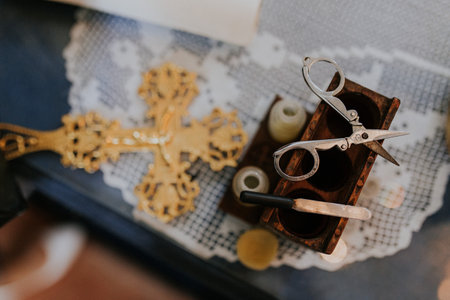 A top view of vintage scissors and a blade on a wooden object on the table next to a golden cross
