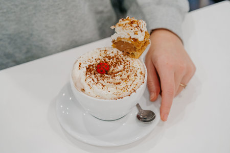 A female hand holding a cup of coffee decorated with whipped creamの写真素材