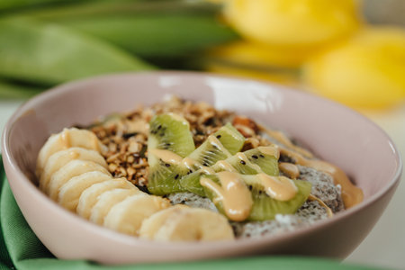 A shot of chia pudding breakfast dish with fresh kiwi and banana with a yellow tulip in background.の写真素材