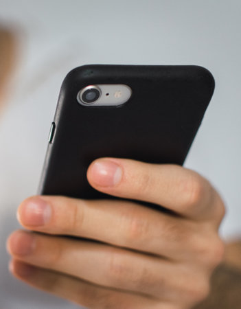 A vertical shot of a smartphone with a black phone case held by a male handの写真素材