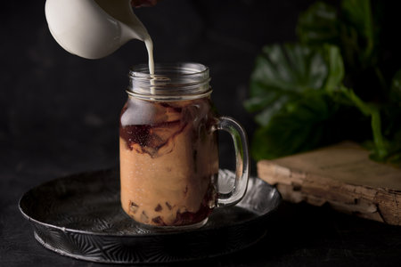 A shot of a hand pouring milk in a jar with coffeeの写真素材