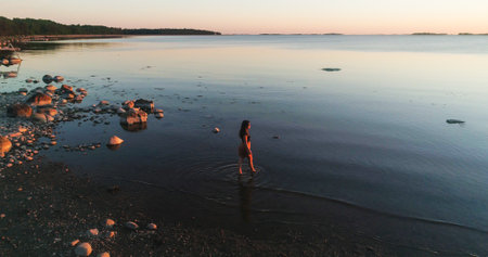 Woman walking in the water, aerial view around a on a girl enjoying a warm sunset and calming her feets in the sea, sunny summer evening duskの写真素材