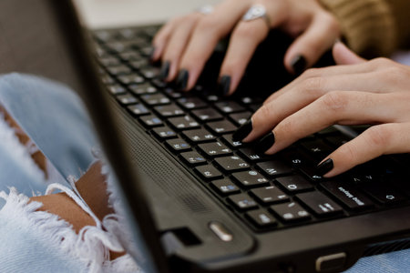 A closeup of female hands typing on a black laptopの写真素材
