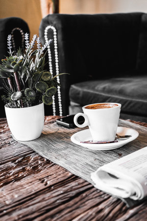 A vertical shot of a cup of fresh morning coffee and a potted plant on a tableの写真素材