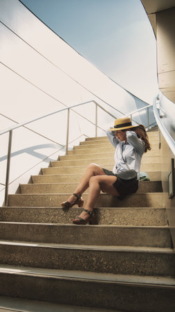 An African-American female wearing a shirt with a skirt and sitting on stairs in a park in the USAの写真素材