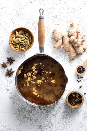 Top View of chai Latte in a pot with spices around to it: cloves, cardamom and ginger