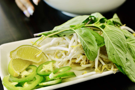 A platter of fresh toppings for Pho - jalapenos, bean sprouts, lime slices, basil, and onionsの写真素材