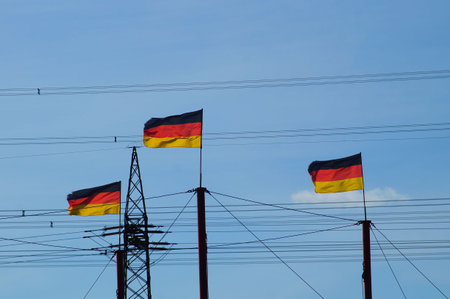 German flags flying in front of a high-voltage road. The expansion of transmission lines is crucial for the restructuring of the energy supply.の写真素材