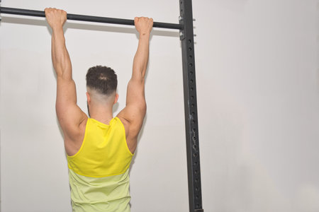 A closeup shot of a white Caucasian man doing pull-ups in the gym