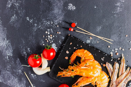 Delicious anchovies and shrimps with garlic and cherry tomatoes on the dark grunge surfaceの写真素材