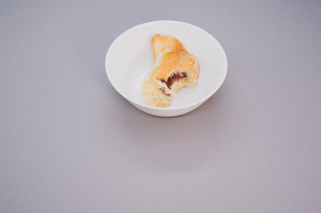 A bitten croissant on a white plate isolated on purple backgroundの写真素材