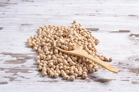 A closeup of raw organic chickpeas with a wooden spoon isolated on the wooden backgroundの写真素材