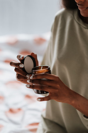 An African female holding a glass jar with a handmade scented candle in her roomの写真素材