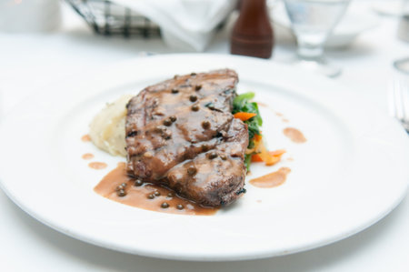 A closeup shot of a steak with sauce and greens on a white plateの写真素材
