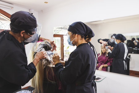 A closeup shot of Hispanic hairdressers colors the hair of a young woman in the beauty salonの写真素材