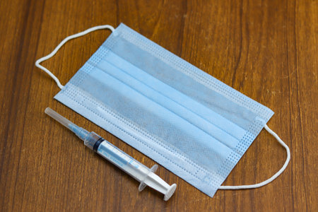 A syringe and a face mask on a wooden background - Covid-19 pandemicの写真素材