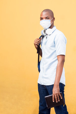 A young Afro American with a medical mask and earphones posing at camera on a yellow backgroundの写真素材