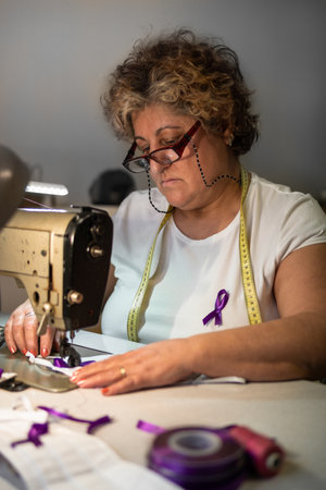 A shallow focus of an adult Spanish woman sewing a purple ribbon on a facemask - COVID-19の写真素材