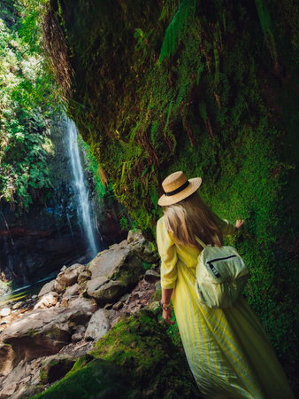 A cute blond woman with a summer hat admiring foamy waterfall over rocks in the forest on a sunny...
