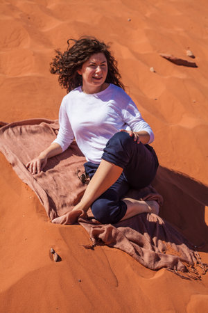 A vertical caucasian female with curly hair posing on the sand in a desertの写真素材