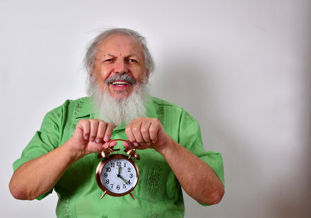 A Caucasian male with green shirt holding an alarm clock on white backgroundの写真素材