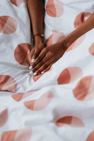 Young African female hands with white manicure on a bed