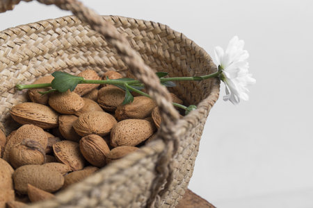 closeup of a wicker basket full of whole almonds on them there is a white flower, the background is white, horizontal photoの写真素材