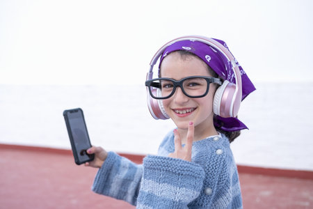 A little Caucasian girl in headphones and glasses doing a selfieの写真素材