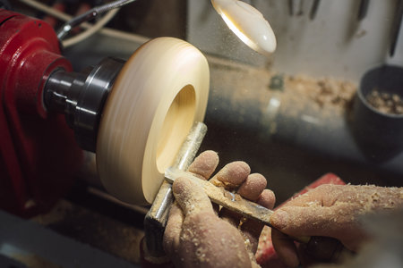 A joinery worker shaping a piece of wood on the lathe with wood shavings and dust on his handsの写真素材
