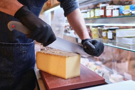 A male staff slicing a block of cheese in a local supermarketの写真素材