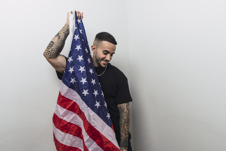 A young Spanish male with tattooed arms posing with an American flag isolated on a white backgroundの写真素材