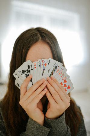 A vertical shot of a girl hides behind playing cardsの写真素材