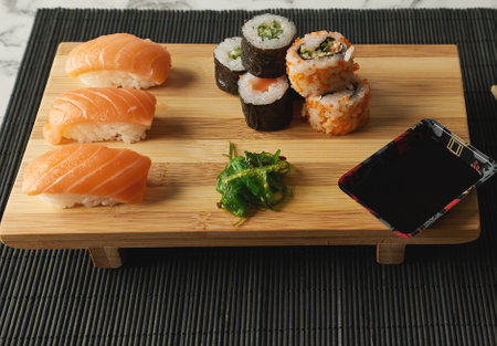 A serving of delicious sushi rolls, salmon sushi, herbs, soy sauce on a wooden boardの写真素材