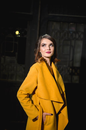 A vertical shot of a young blonde female model in a fashionable yellow coatの写真素材