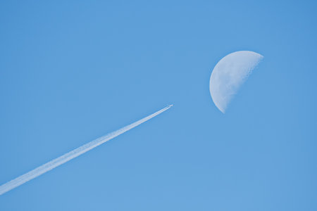 An airplane flying with a trail near the moon